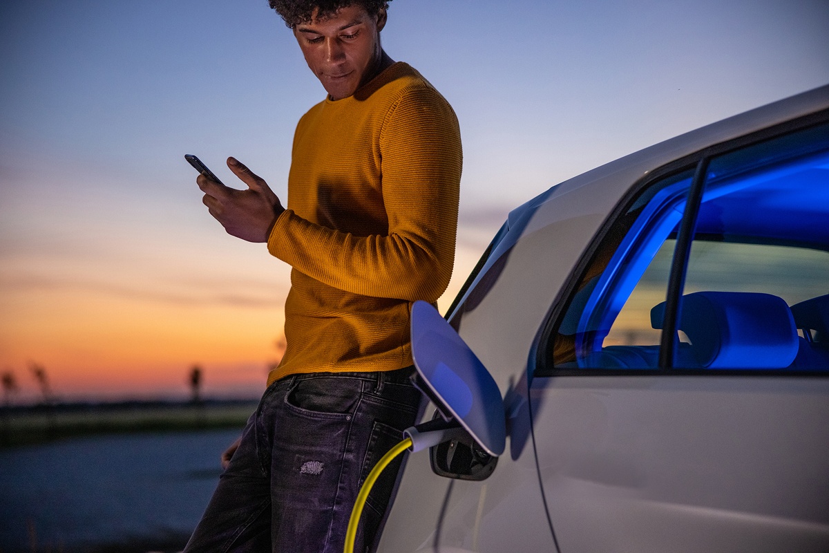 Image of young man leaning on electric vehicle while charging his car